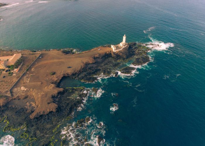 Aerial photos of Farol da Praia in Santiago, Cape Verde showcase a stunning lighthouse on a rugged coastline with breathtaking views of the Atlantic Ocean, surrounded by dramatic cliffs, sandy beaches